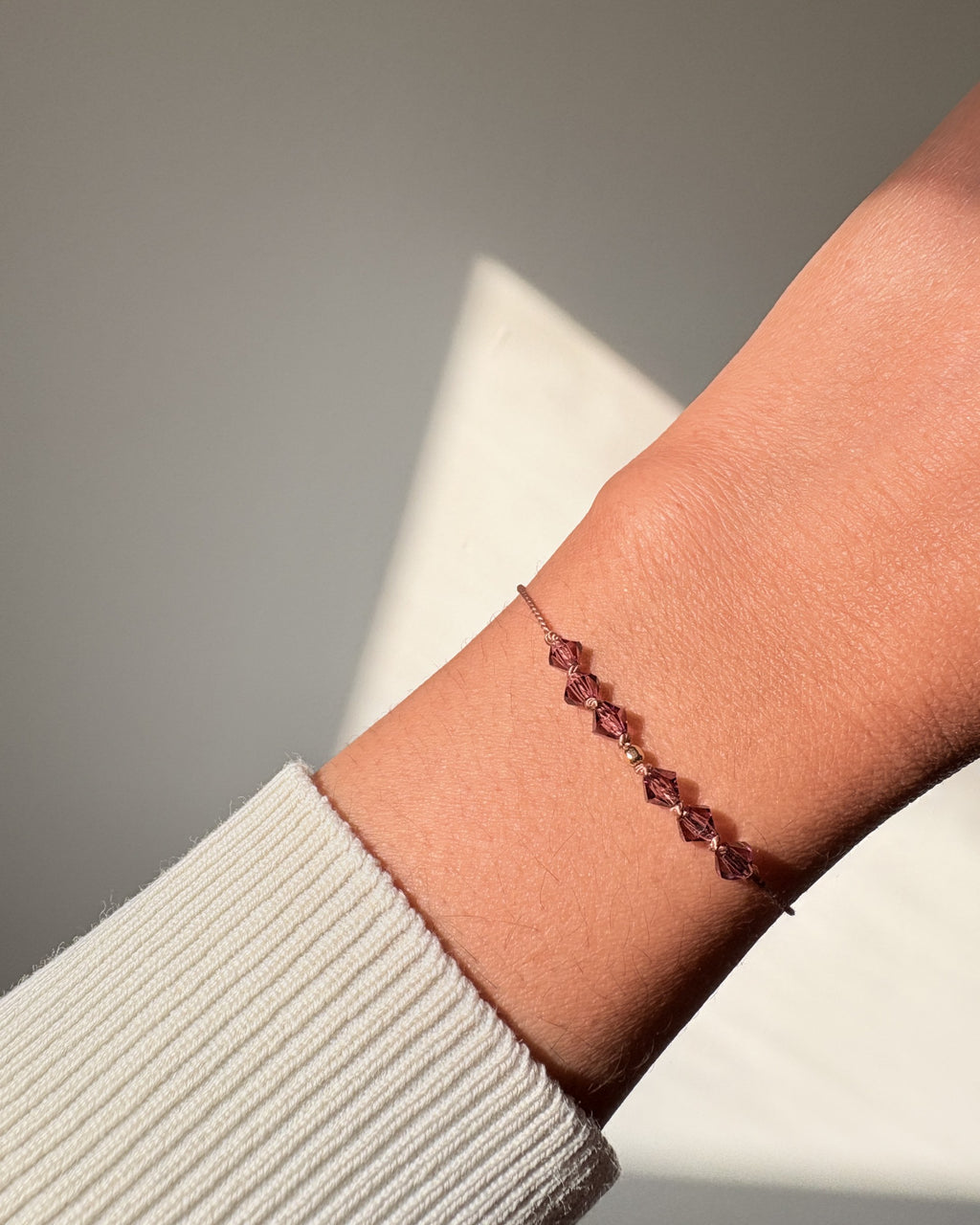Quiet Strength bracelet worn on the wrist in natural light, showing deep purple Amethyst crystals and beige silk cord.