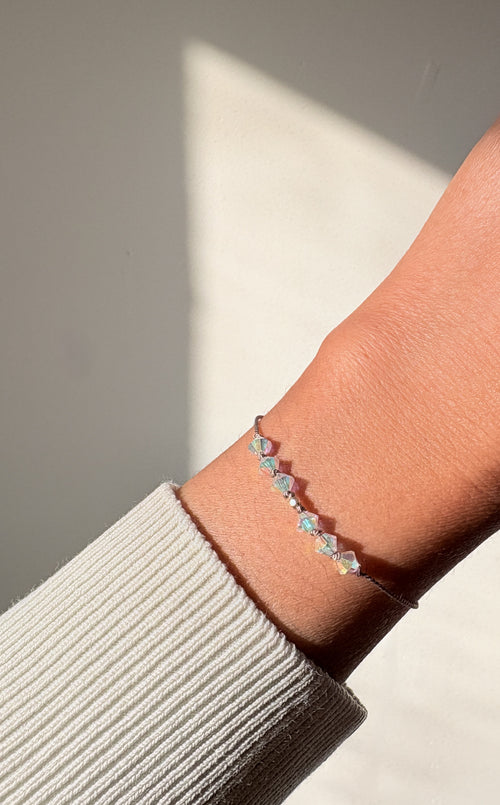 Eternal Hope bracelet worn on the wrist in natural light, showing iridescent Crystal AB crystals and beige silk cord.