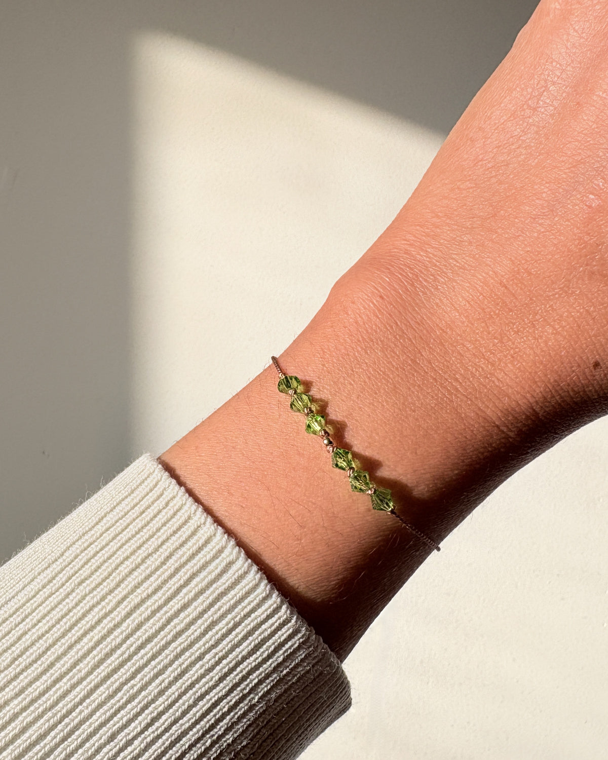 Renewal bracelet worn on the wrist in natural light, showing green Peridot crystals and beige silk cord