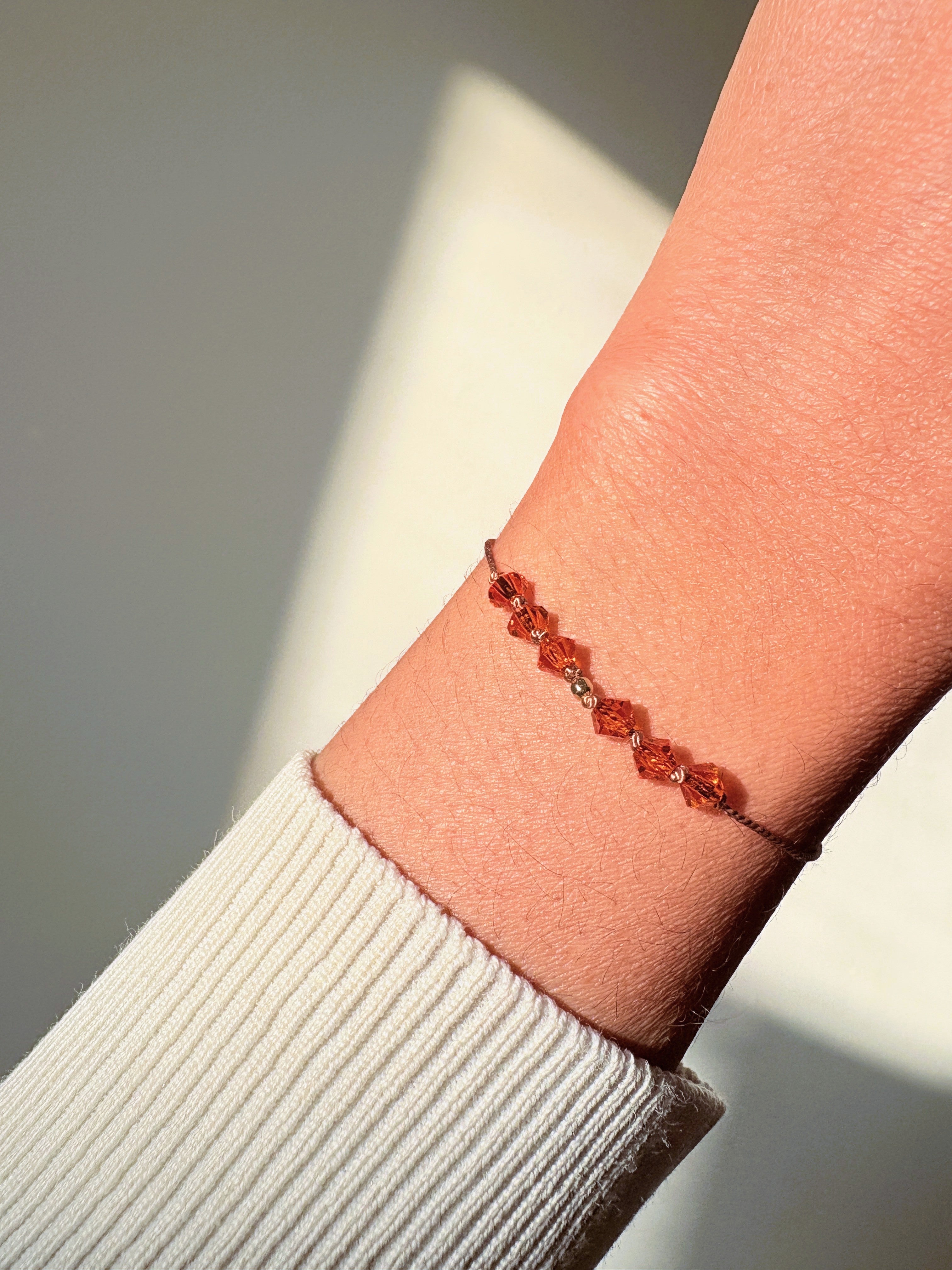 Radiant Hope bracelet worn on the wrist in natural light, showing bright orange Sun crystals and beige silk cord.