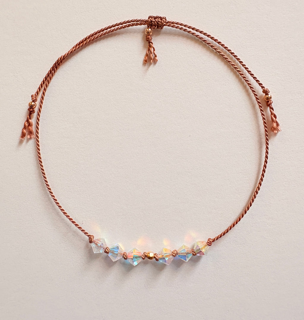 Eternal Hope adjustable bracelet with iridescent Crystal AB crystals, beige silk cord, and gold-filled details on an ivory background.