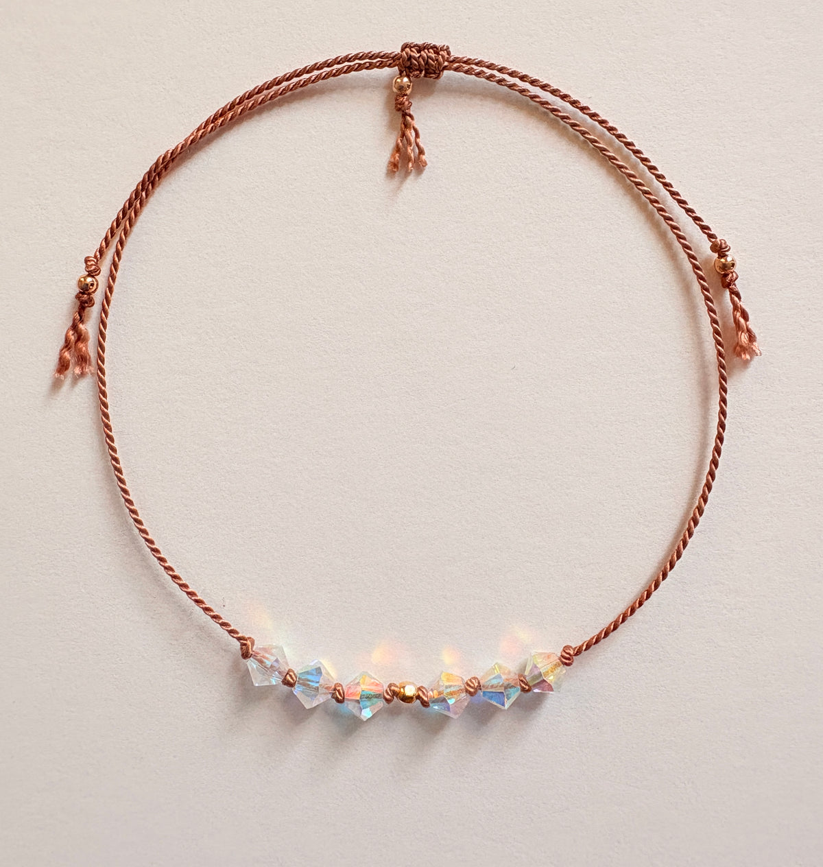 Eternal Hope adjustable bracelet with iridescent Crystal AB crystals, beige silk cord, and gold-filled details on an ivory background.