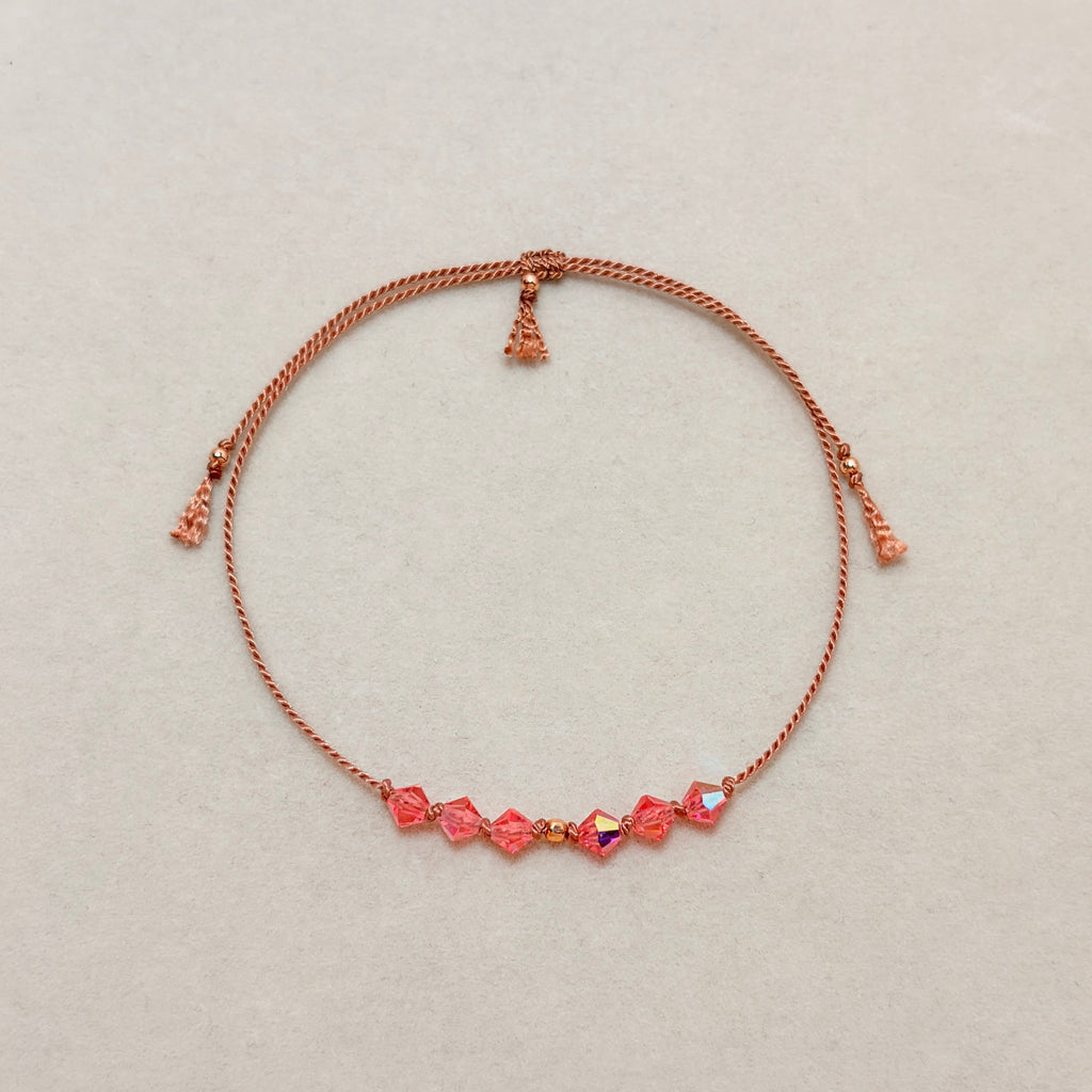 Golden Memory adjustable bracelet with Rose Peach AB crystals, beige silk cord, and gold-filled details on a soft ivory velvet background.