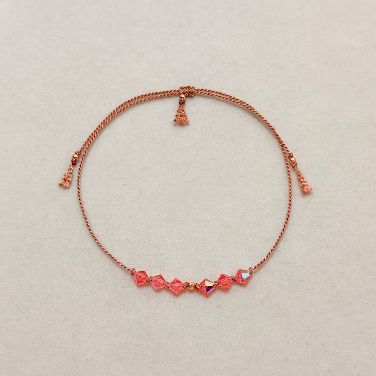 Golden Memory adjustable bracelet with Rose Peach AB crystals, beige silk cord, and gold-filled details on a soft ivory velvet background.