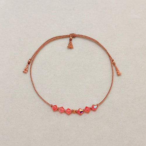 Golden Memory adjustable bracelet with Rose Peach AB crystals, beige silk cord, and gold-filled details on a soft ivory velvet background.