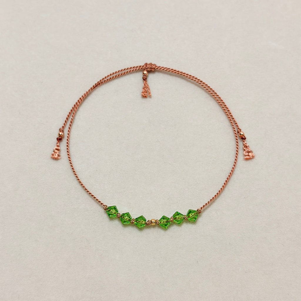 Renewal adjustable bracelet with green Peridot crystals, beige silk cord, and gold-filled details on a soft ivory velvet background.