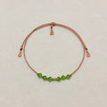 Renewal adjustable bracelet with green Peridot crystals, beige silk cord, and gold-filled details on a soft ivory velvet background.