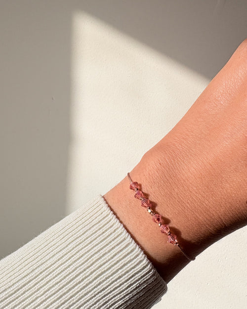 Golden Memory bracelet worn on the wrist in natural light, showing Rose Peach AB crystals and beige silk cord.